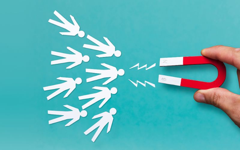 white paper cut-out figures on a teal background being drawn in by a magnet