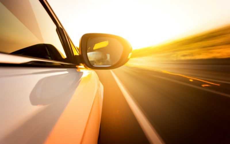 vehicle driving down road bathed in golden sunlight