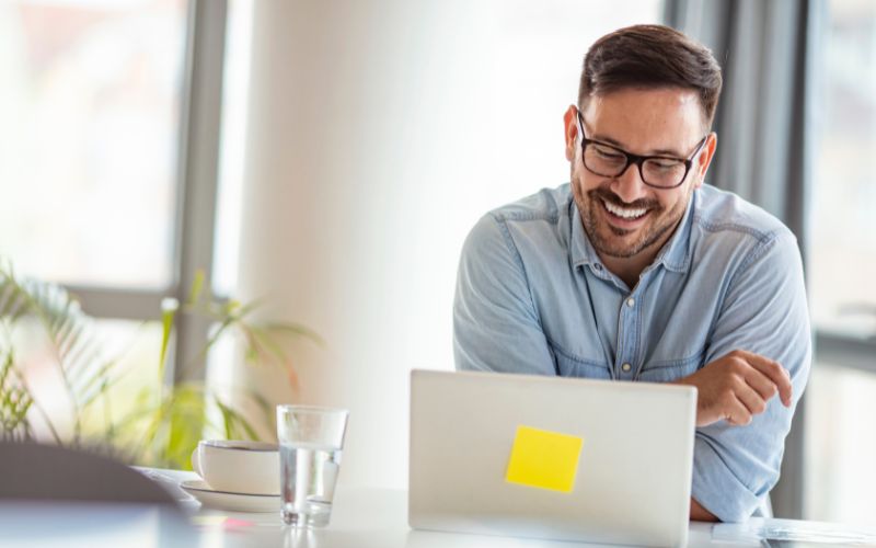 Man in professional casual dress smiling behind computer monitor