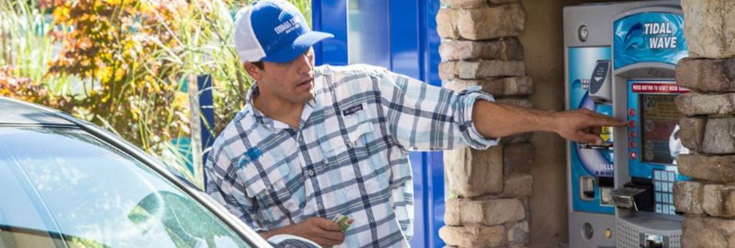 car wash attendant pointing to a pay station screen while talking with a customer in a car