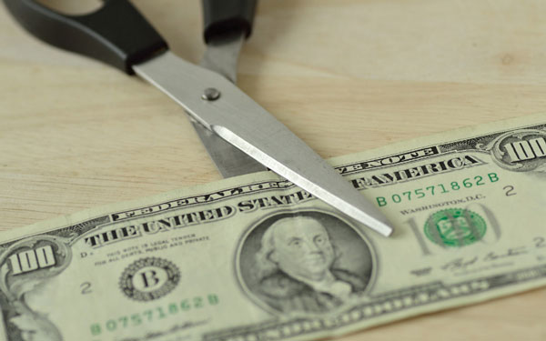 One hundred dollar bill sitting on a beige table top sitting inside scissors as if being cut in half