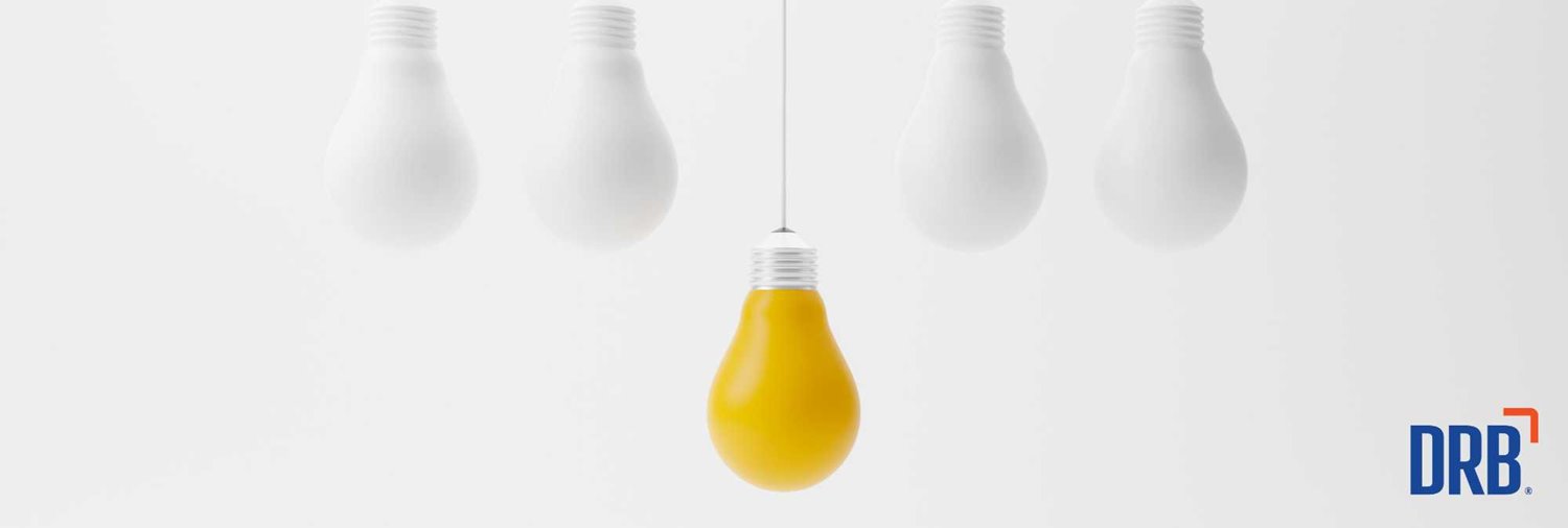 light blubs suspended on white background with a yellow light bulb hanging lower than the others