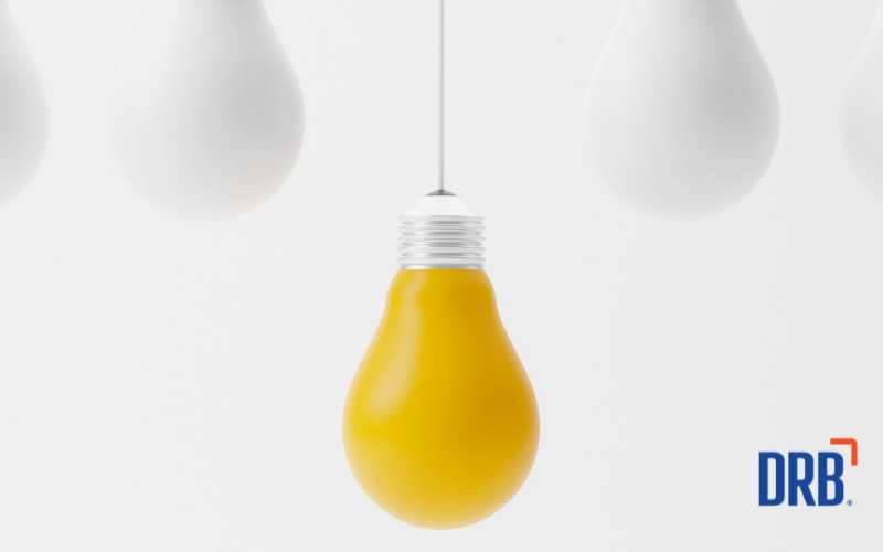 light blubs suspended on white background with a yellow light bulb hanging lower than the others