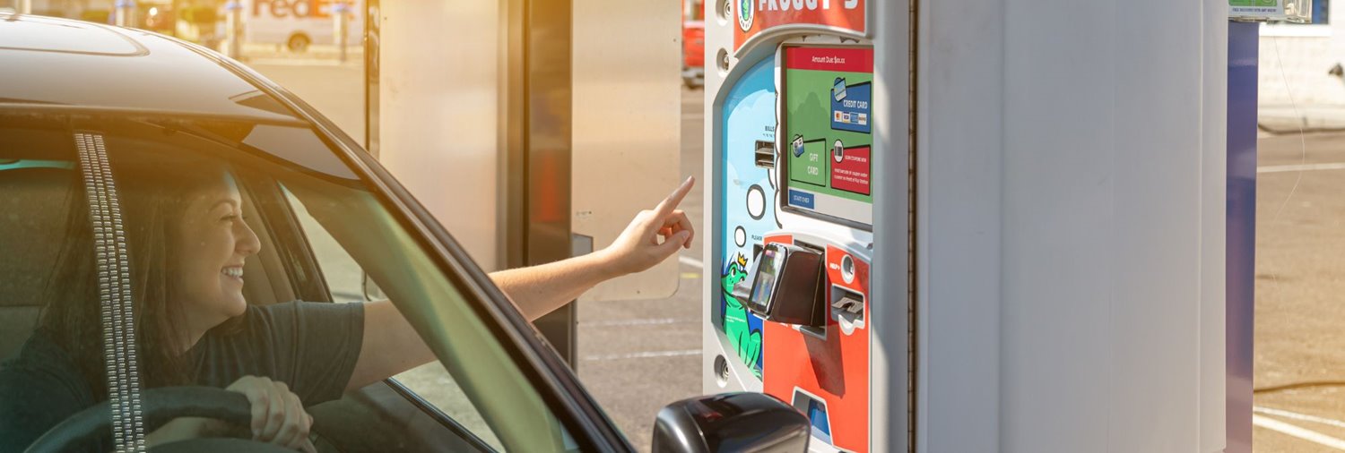 a smiling woman in a car reaching out to a pay station