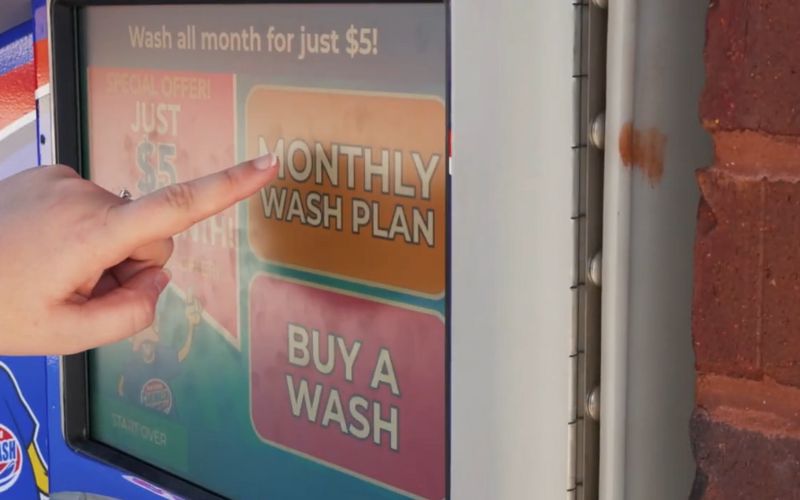 Finger reaching out to touch monthly wash plan option on car wash pay station screen