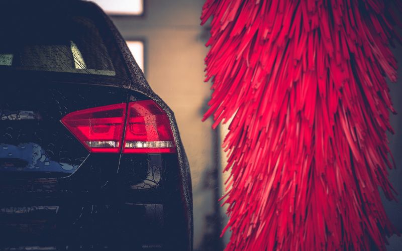 wet passenger side taillight of a black car going by a red car wash wrap