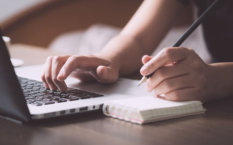person taking notes while looking at computer