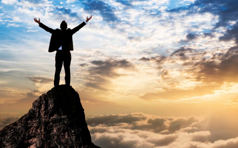 Man with arms in air on top of a mountain