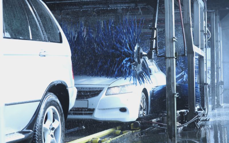 white sedan going through car wash as top wrap cleans the hood 