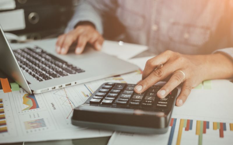 close up of a person's hands with one on a laptop keyboard and the other on a calculator