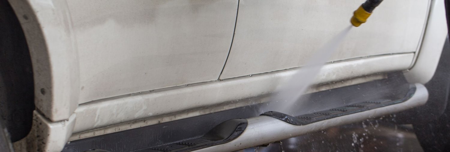 bottom side of a white car being sprayed by a car wash prep gun