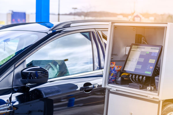 Black car driving up beside a drb outdoor touch terminal at a car wash