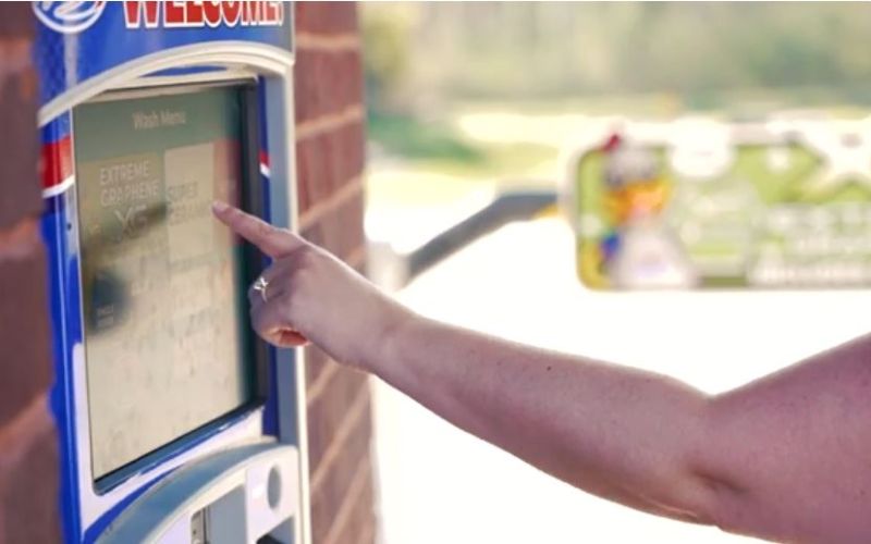 woman's hand reaching to touch a car wash pay station screen