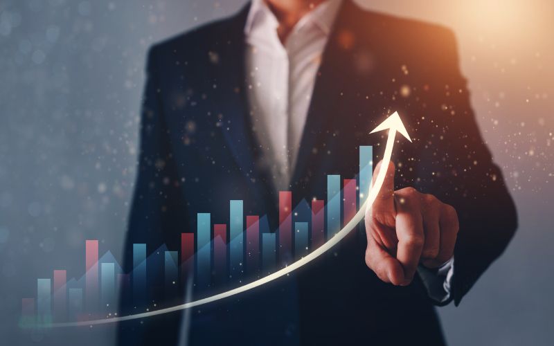 man standing in front of a clear screen gesturing toward a graph an upward trajectory