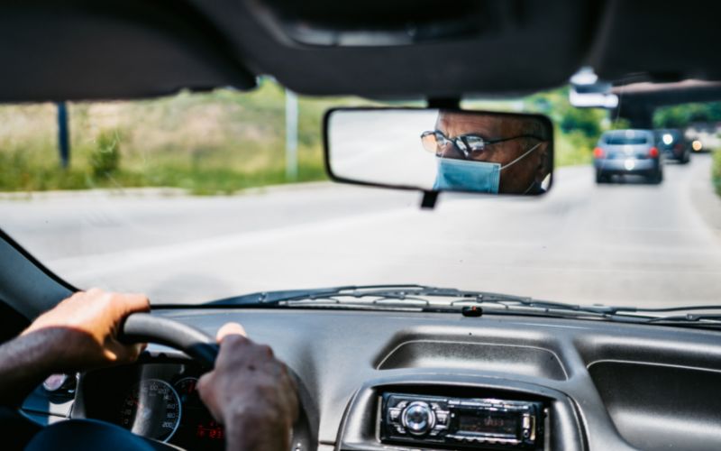 reflection in rear view mirror of a man wearing a mask