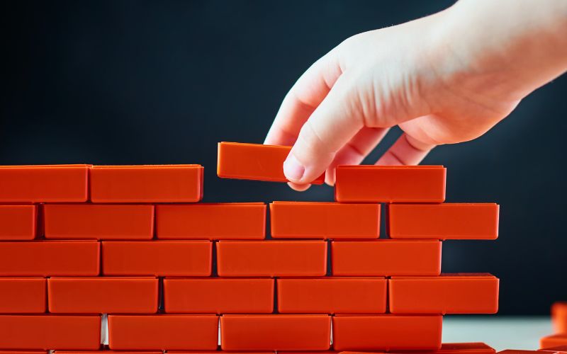 hand setting a red block on a wall of other red blocks