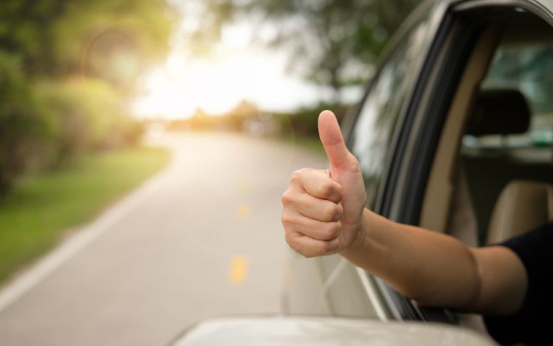 close up of someone giving a thumbs up outside a vehicle going down the road