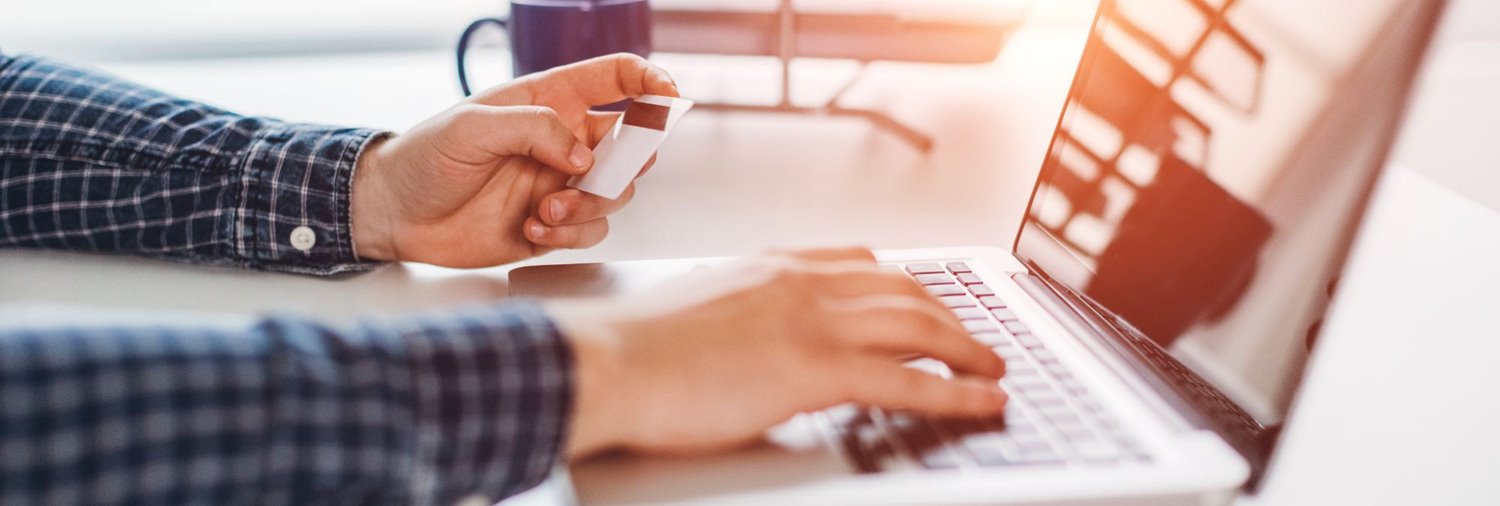 person's hand holding a credit card while typing on a laptop