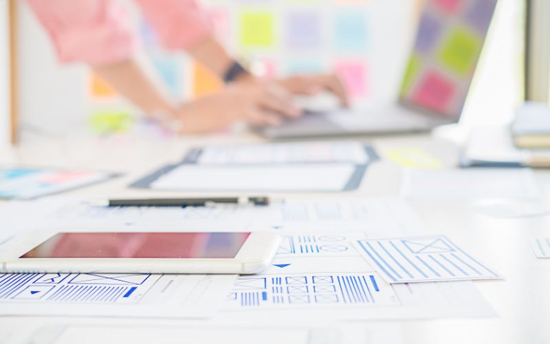 a tablet on top of website wireframes with a blurred image of a man working on a computer in the background