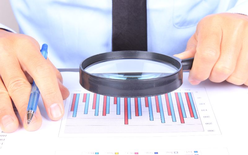 hand holding magnifying glass focused on report with bar graph