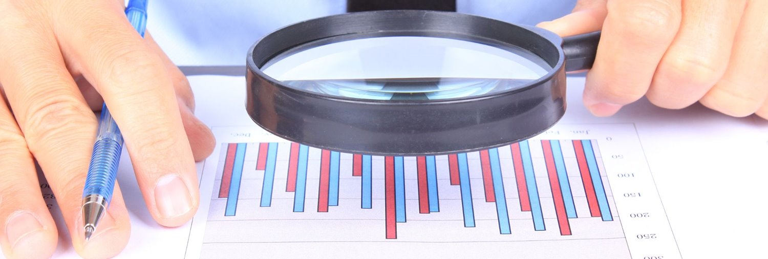 hand holding magnifying glass aimed at report with bar graph