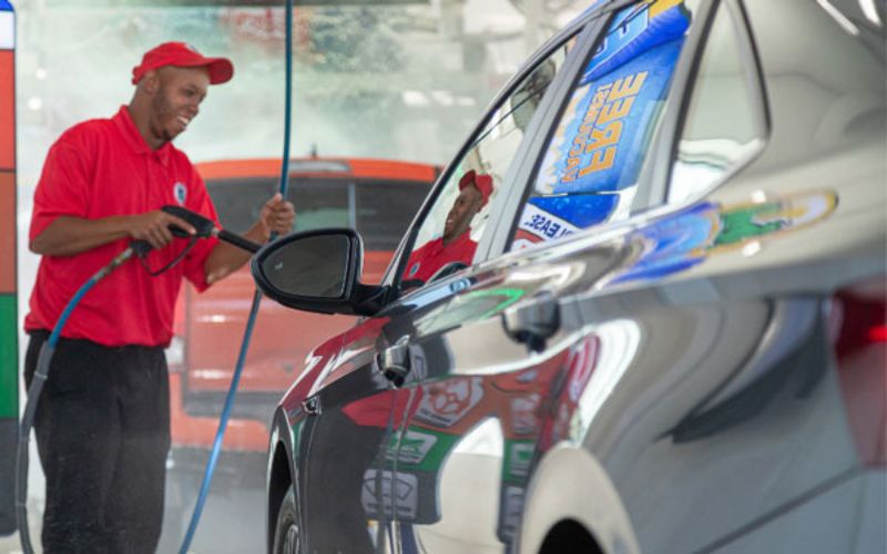 car wash attendant spraying a vehicle entering the tunnel