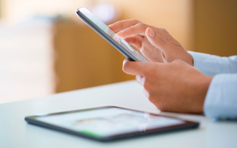 a man's hands holding a smartphone at a white table with a tablet sitting on the table