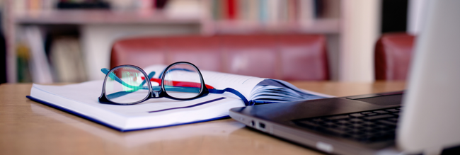 glasses sitting on a notebook in front of a laptop computer